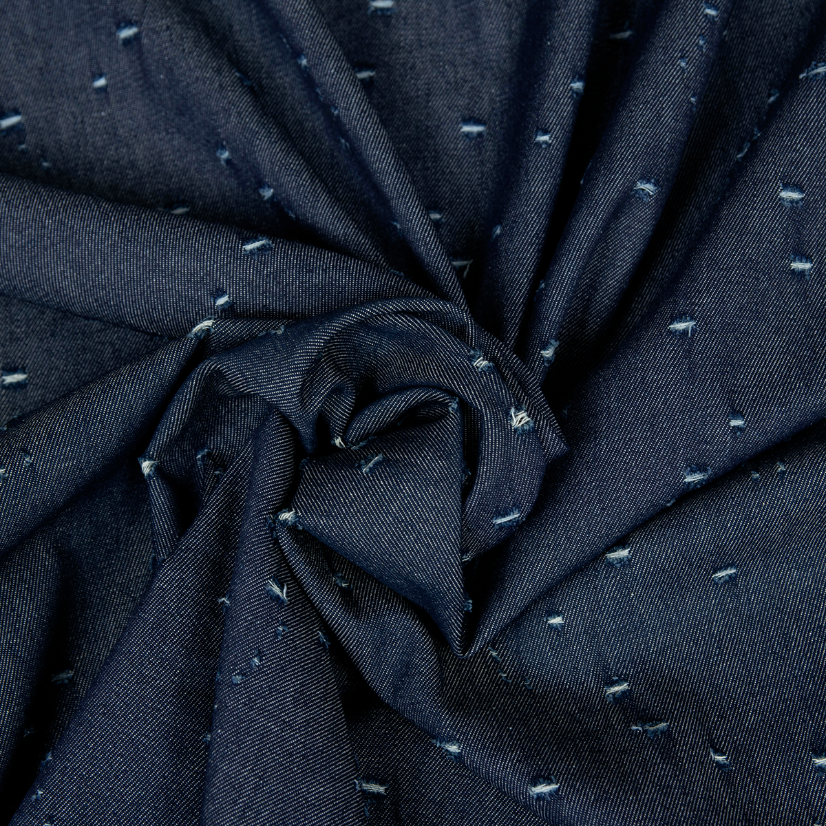Tessuto jeans blu scuro con fori decorativi irregolari e fibre chiare a contrasto.
