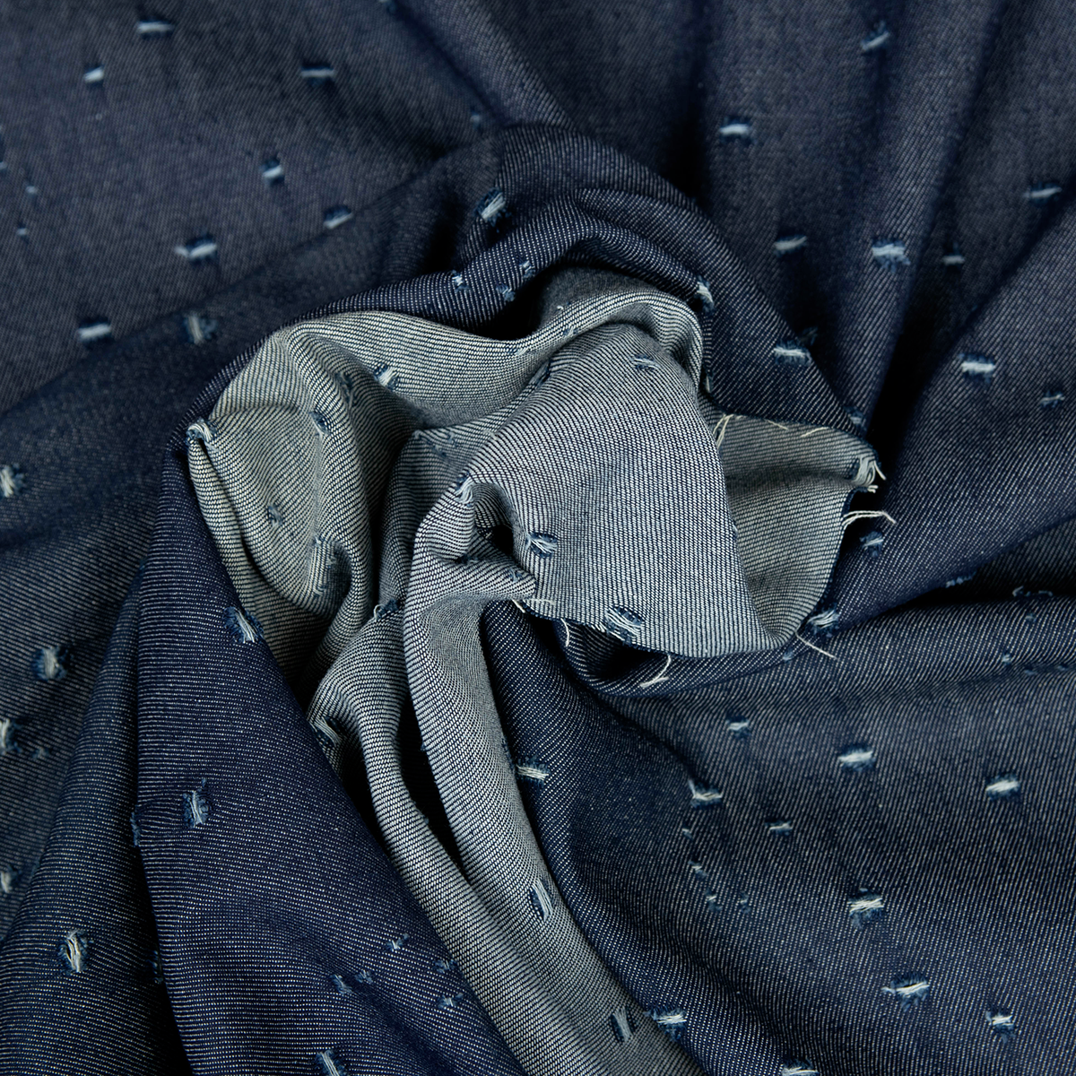 Dettaglio denim blu indigo con lavorazione traforata al laser ed effetto sfrangiato.