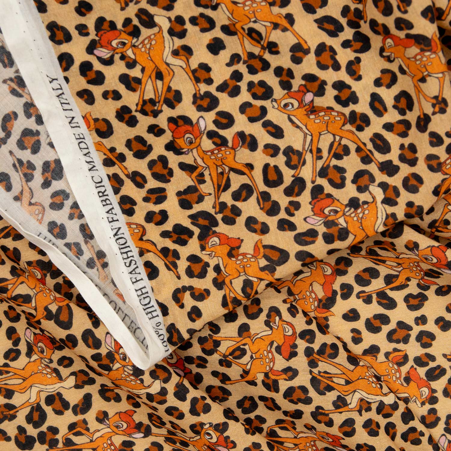 Mussola di cotone stampata Made in Italy con fantasia Bambi animalier su fondo sabbia, drappeggiata con etichetta di bordo visibile