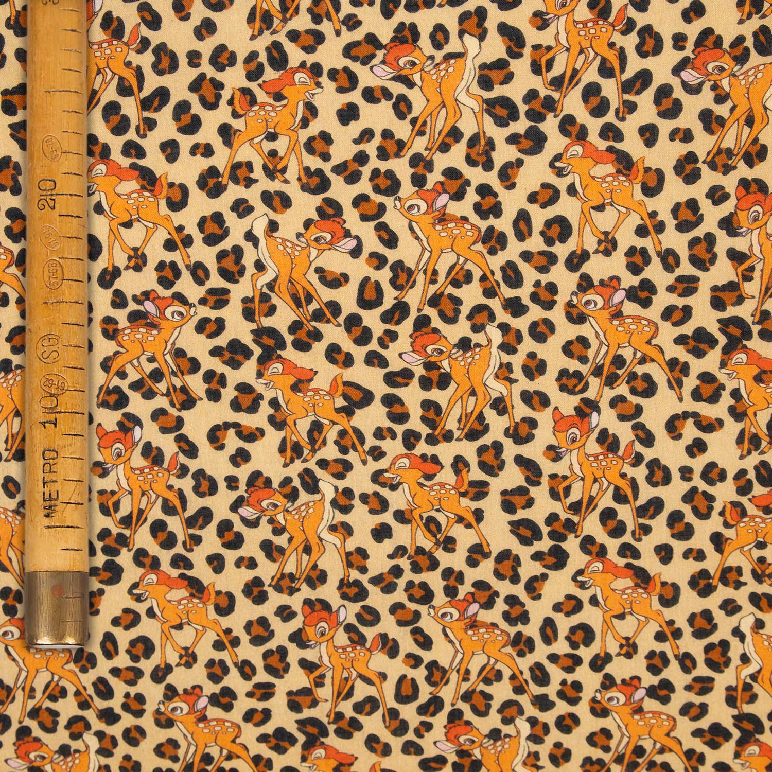 Mussola di cotone stampata fantasia Bambi leopardato stesa in piano con metro da sarto per indicare la larghezza del tessuto
