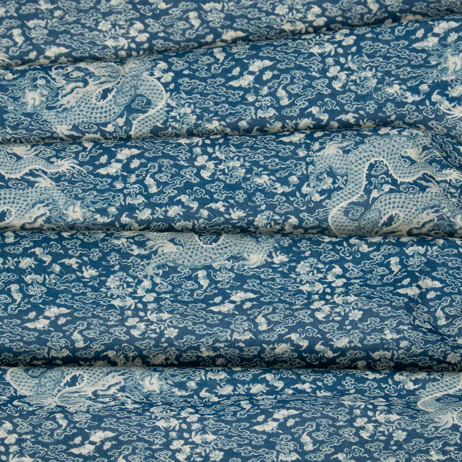 Mussola di cotone stampata deadstock con motivo dragoni orientali su fondo blu petrolio, tessuto piegato in più strati
