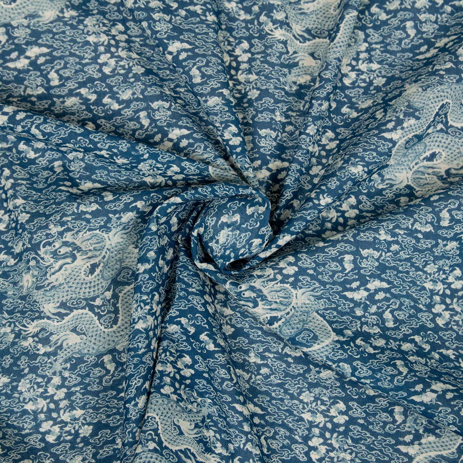 Dettaglio mussola cotone 100% con stampa dragoni cinesi blu e bianco, tessuto morbido arrotolato che mostra la caduta e la leggerezza del filato