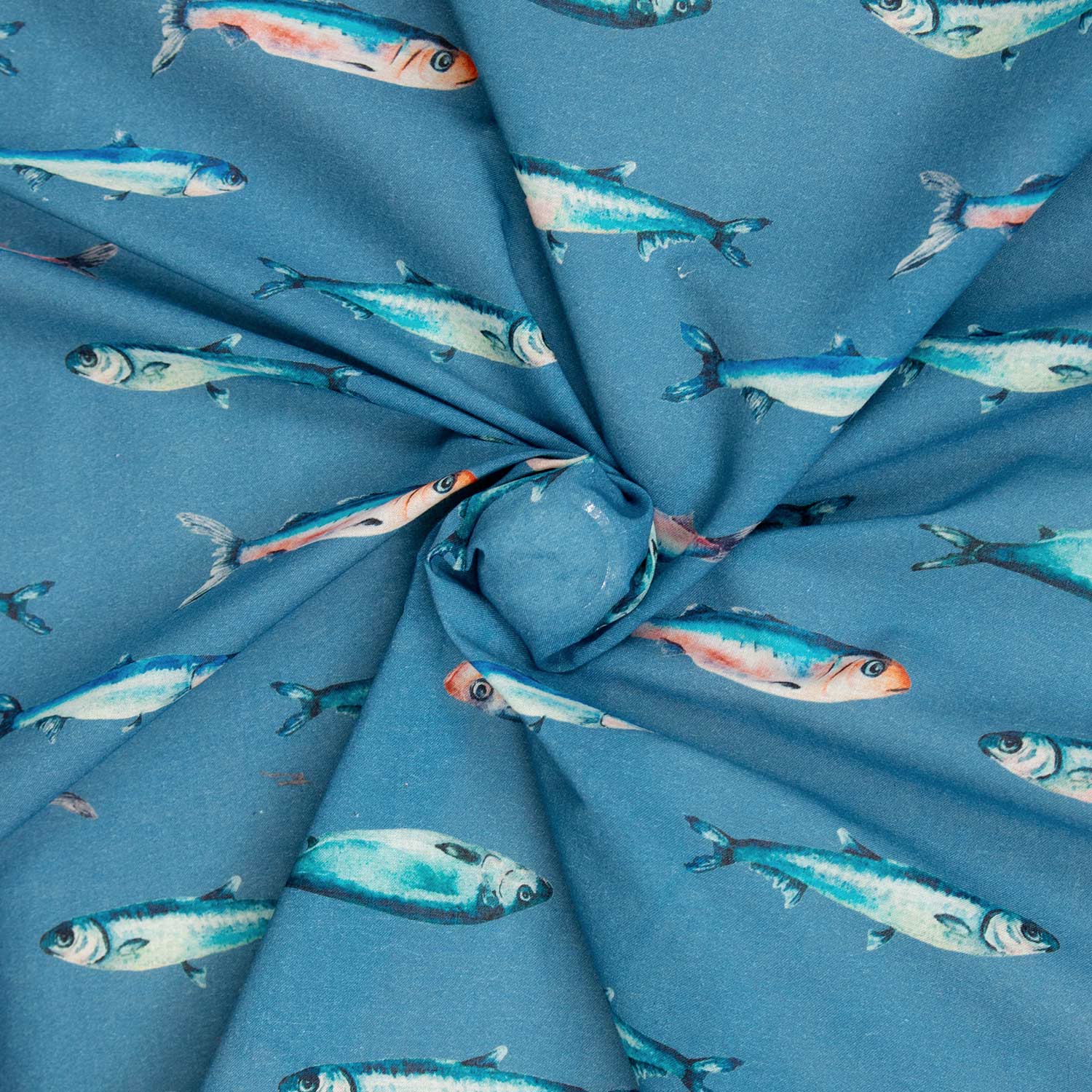 Dettaglio mussola cotone deadstock con motivo a sardine teal e corallo su fondo blu, tessuto morbido arrotolato che mostra la caduta fluida e la leggerezza del cotone estivo