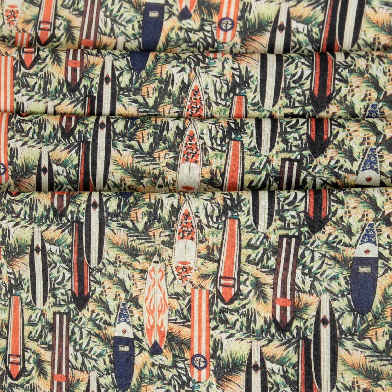 Dettaglio mussola cotone leggera con stampa surf retrò e foglie tropicali, tessuto deadstock piegato in più strati che mostra la densità del pattern e la consistenza del cotone estivo