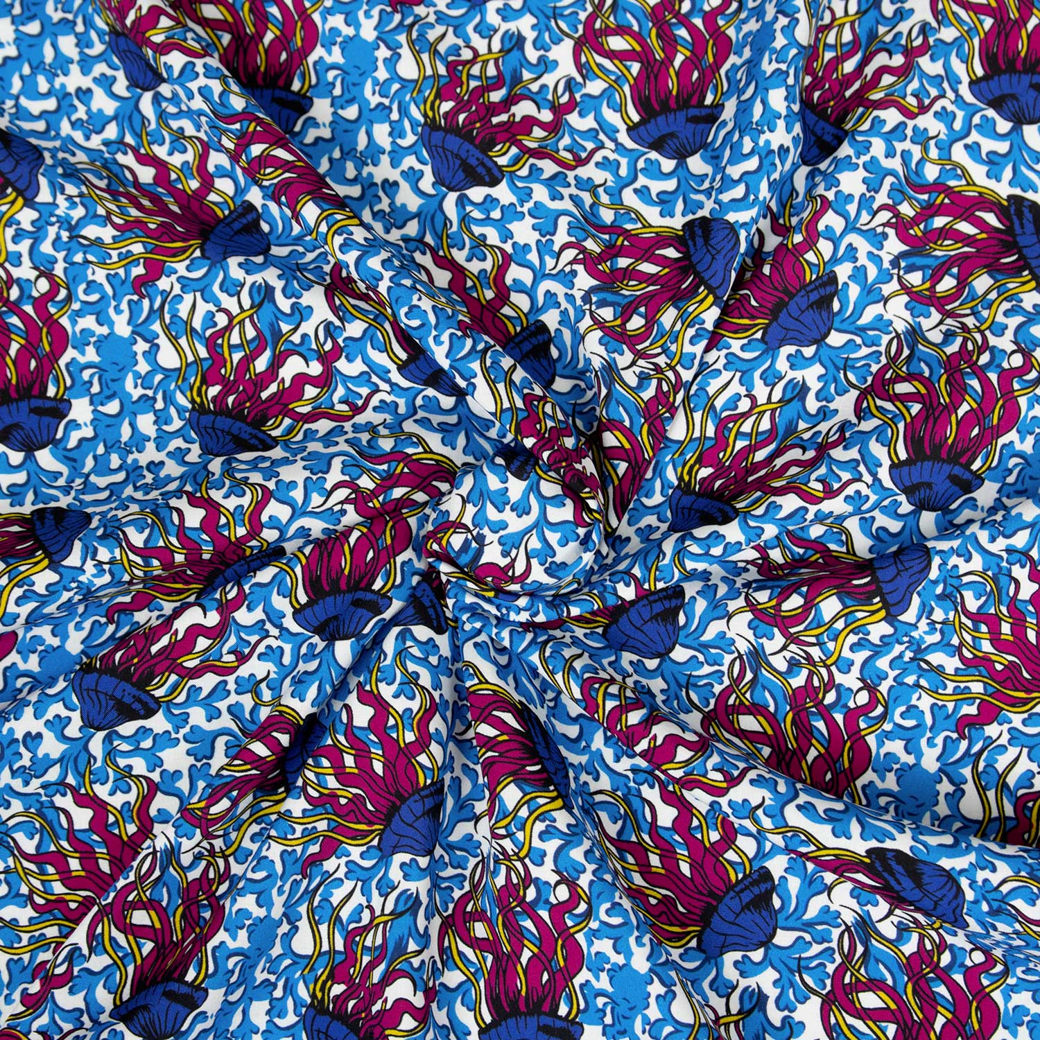 Dettaglio mussola cotone stampata deadstock con pattern meduse stile wax africano in blu, fucsia e giallo, tessuto arrotolato che mostra la caduta fluida e la leggerezza del cotone traspirante